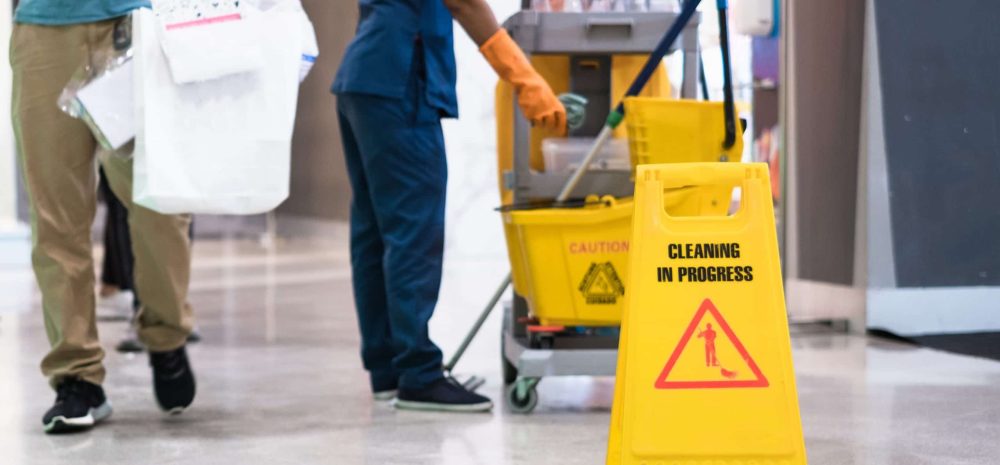 Janitor Cleaning Floor In Front Of Yellow Caution "Cleaning in progress". Cleaning service in public area.